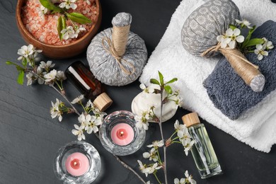 Photo of Spa composition with cosmetic products, burning candles and beautiful flowers on black textured table, flat lay