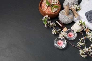 Photo of Spa composition with cosmetic products, burning candles and beautiful flowers on black textured table, above view. Space for text