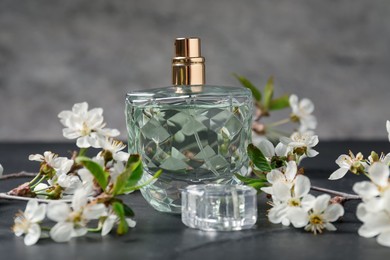 Photo of Bottle of aromatic perfume and twigs with beautiful flowers on gray background, closeup