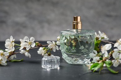 Photo of Bottle of aromatic perfume and twigs with beautiful flowers on gray background, closeup
