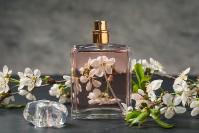 Photo of Bottle of aromatic perfume and twigs with beautiful flowers on gray background, closeup