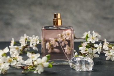 Photo of Bottle of aromatic perfume and twigs with beautiful flowers on gray background, closeup