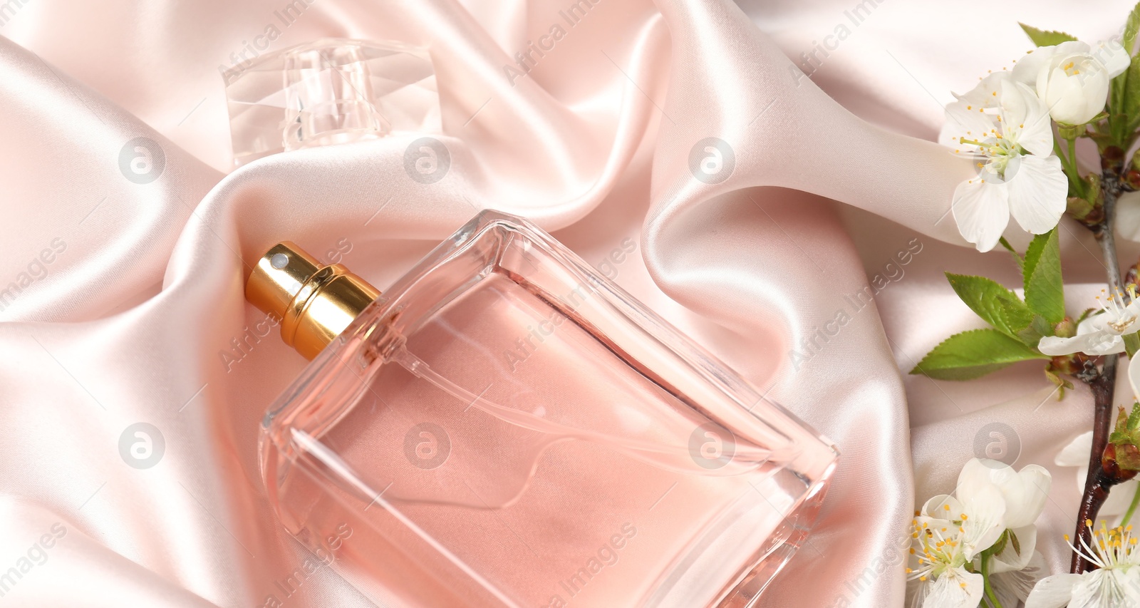 Bottle of aromatic perfume and twig with beautiful flowers on beige silk fabric, closeup Photo of Bottle of aromatic perfume and twig with beautiful flowers on beige silk fabric, closeup