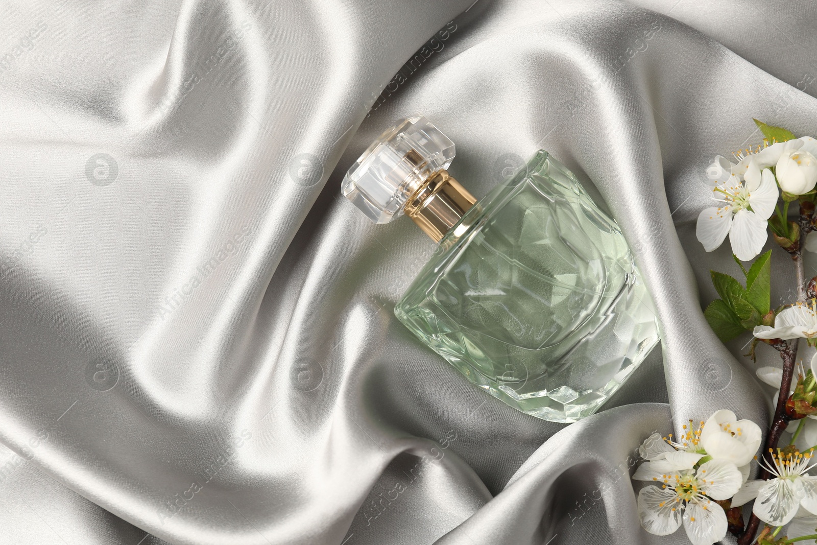 Bottle of aromatic perfume and twig with beautiful flowers on gray silk fabric, flat lay. Space for text Photo of Bottle of aromatic perfume and twig with beautiful flowers on gray silk fabric, flat lay. Space for text