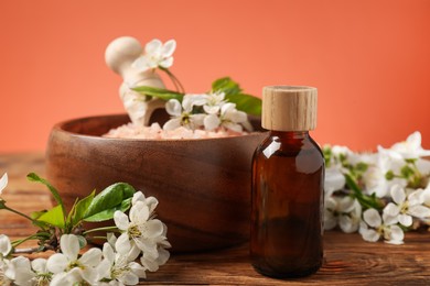 Photo of Spa composition with sea salt, bottle of cosmetic product and beautiful flowers on wooden table against coral background, closeup