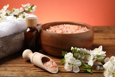 Photo of Spa composition with sea salt, cosmetic product and beautiful flowers on wooden table, closeup