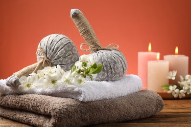 Photo of Spa composition with herbal bags, beautiful flowers and burning candles on wooden table against coral background, closeup