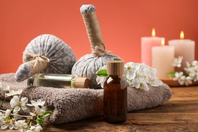 Photo of Spa composition with cosmetic products, beautiful flowers and burning candles on wooden table against coral background, closeup