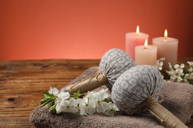 Photo of Spa composition with herbal bags, beautiful flowers and burning candles on wooden table against coral background, closeup. Space for text