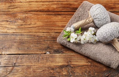 Photo of Herbal bags, towel and twig with beautiful flowers on wooden table, space for text