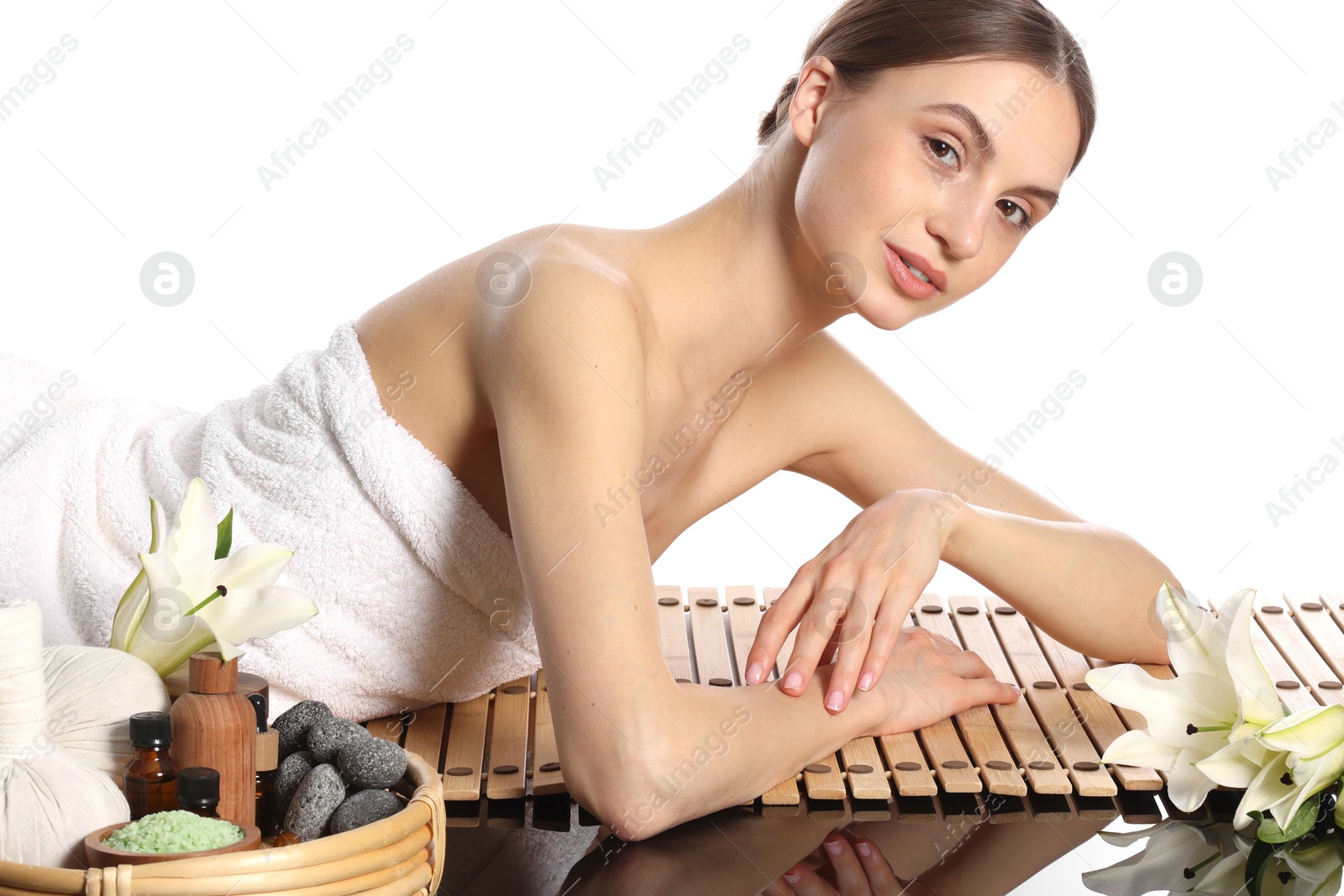 Photo of Beautiful woman posing on bamboo mat against white background. Spa products and flowers on mirror surface