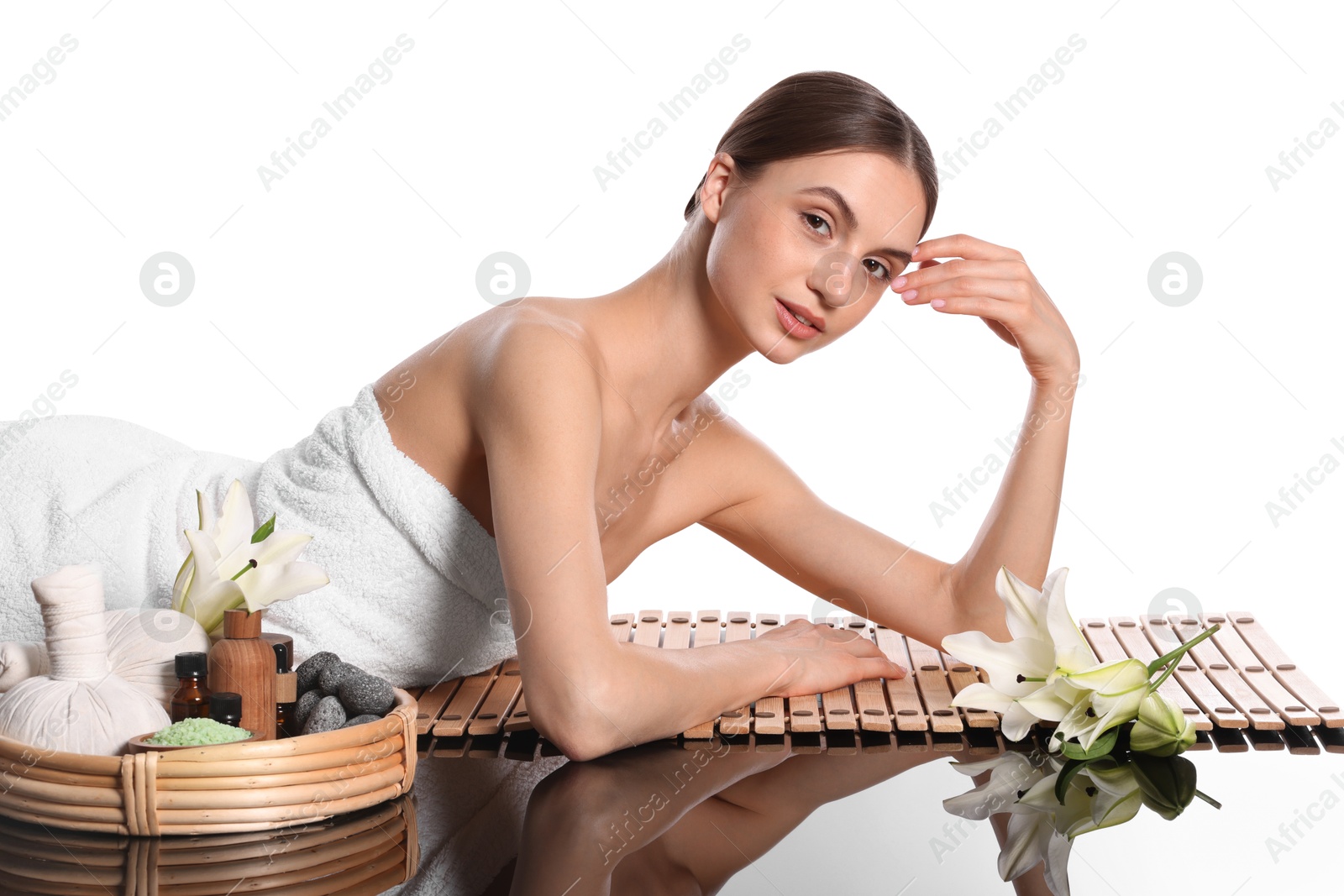 Photo of Beautiful woman posing on bamboo mat against white background. Spa products and flowers on mirror surface