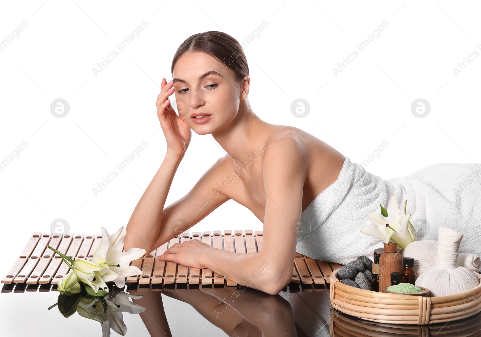 Beautiful woman posing on bamboo mat against white background. Spa products and flowers on mirror surface Photo of Beautiful woman posing on bamboo mat against white background. Spa products and flowers on mirror surface