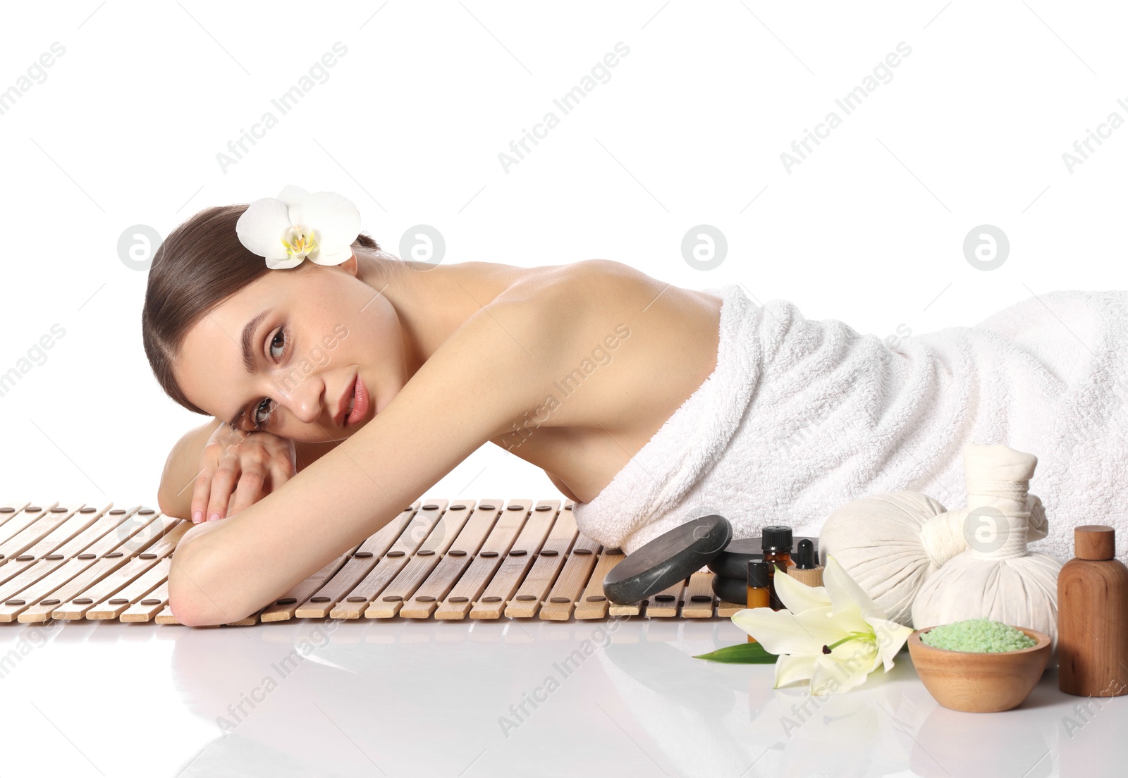 Beautiful woman lying on bamboo mat against white background. Spa products and flowers on mirror surface Photo of Beautiful woman lying on bamboo mat against white background. Spa products and flowers on mirror surface