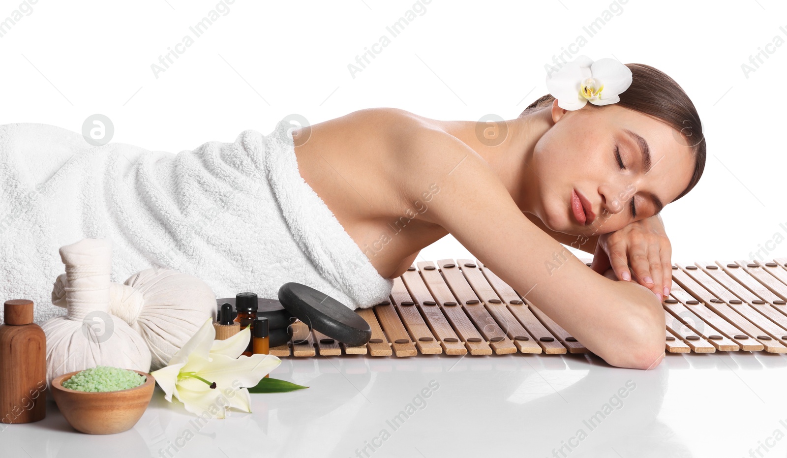 Photo of Beautiful woman lying on bamboo mat against white background. Spa products and flowers on mirror surface