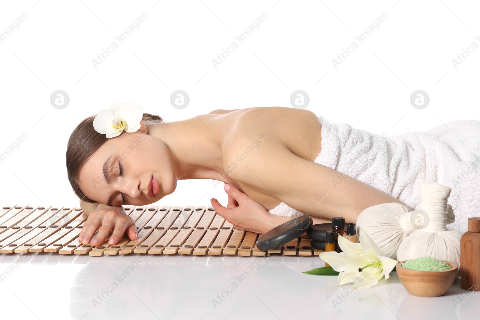 Beautiful woman lying on bamboo mat against white background. Spa products and flowers on mirror surface Photo of Beautiful woman lying on bamboo mat against white background. Spa products and flowers on mirror surface