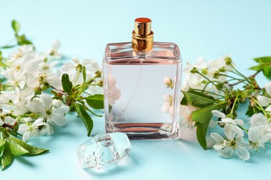 Photo of Bottle of aromatic perfume and twigs with beautiful flowers on light blue background, closeup