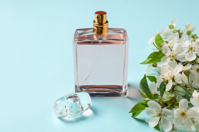 Photo of Bottle of aromatic perfume and twig with beautiful flowers on light blue background, closeup