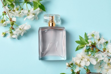 Photo of Bottle of aromatic perfume and twigs with beautiful flowers on light blue background, flat lay