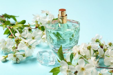 Photo of Bottle of aromatic perfume and twigs with beautiful flowers on light blue background, closeup