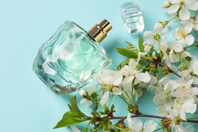 Photo of Bottle of aromatic perfume and twigs with beautiful flowers on light blue background, flat lay