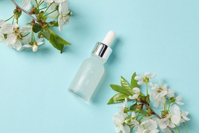 Photo of Bottle of cosmetic product and twigs with beautiful flowers on light blue background, flat lay
