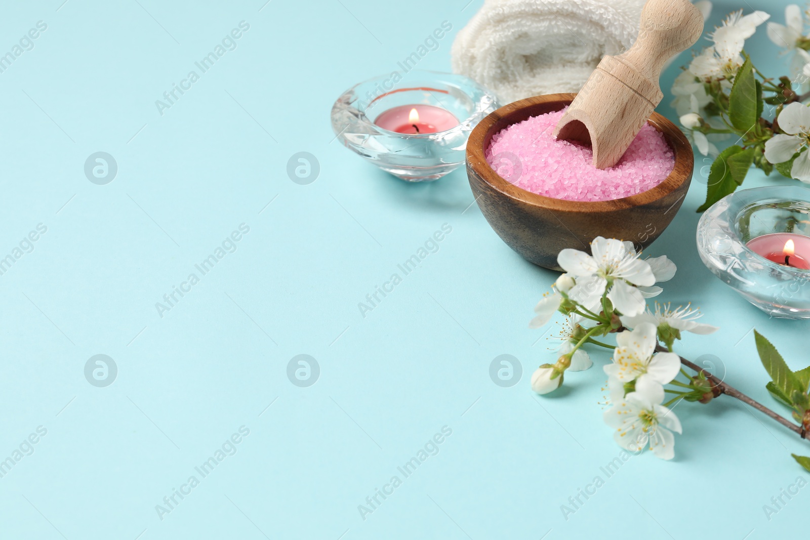 Spa composition with sea salt, burning candles, towel and beautiful flowers on light blue background, space for text Photo of Spa composition with sea salt, burning candles, towel and beautiful flowers on light blue background, space for text