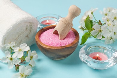 Photo of Spa composition with sea salt, burning candles, towel and beautiful flowers on light blue background, closeup