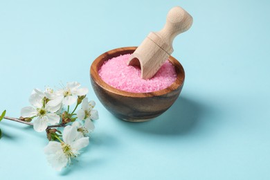 Photo of Sea salt in bowl, scoop and twigs with beautiful flowers on light blue background