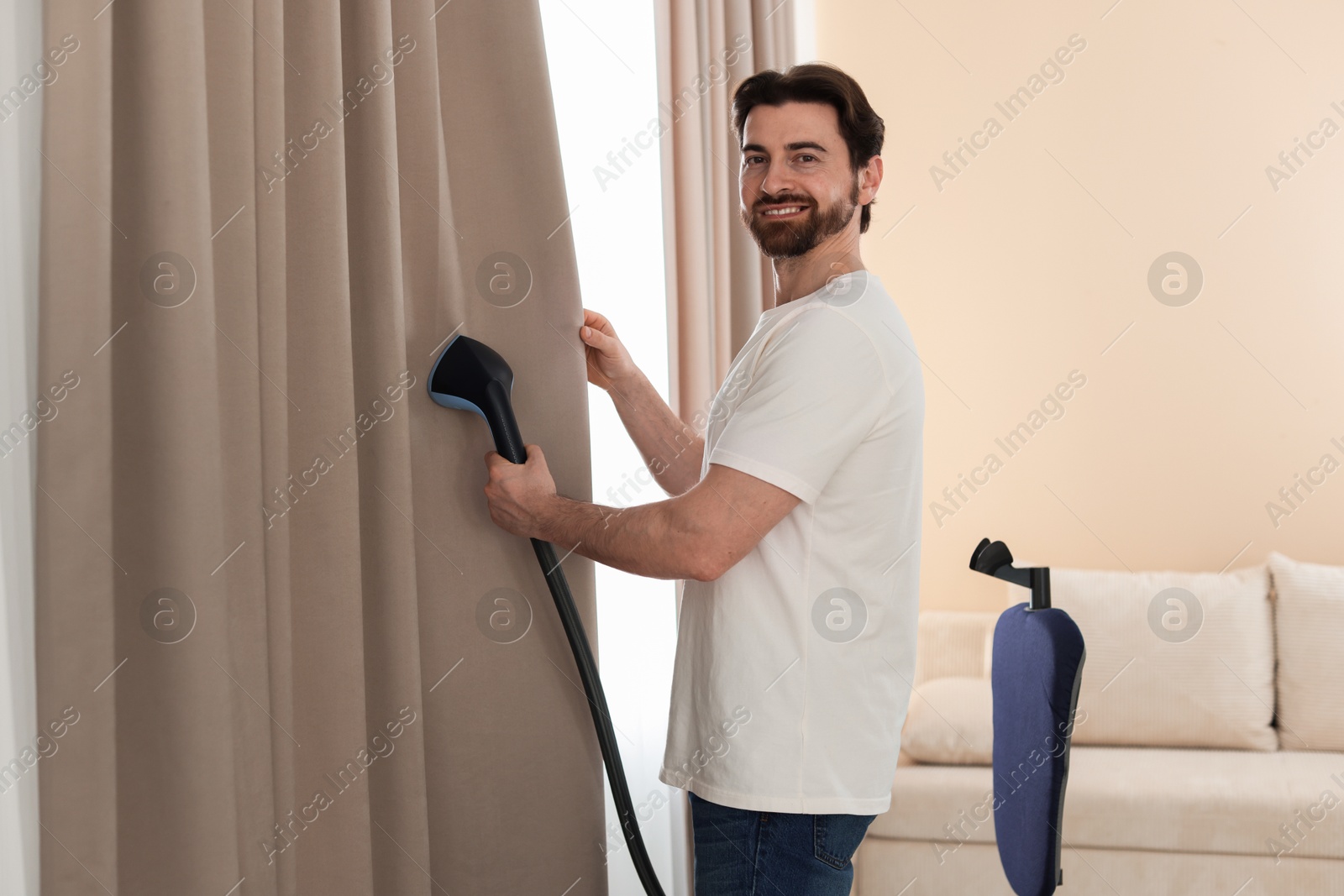 Man steaming curtains with stand steamer at home Photo of Man steaming curtains with stand steamer at home