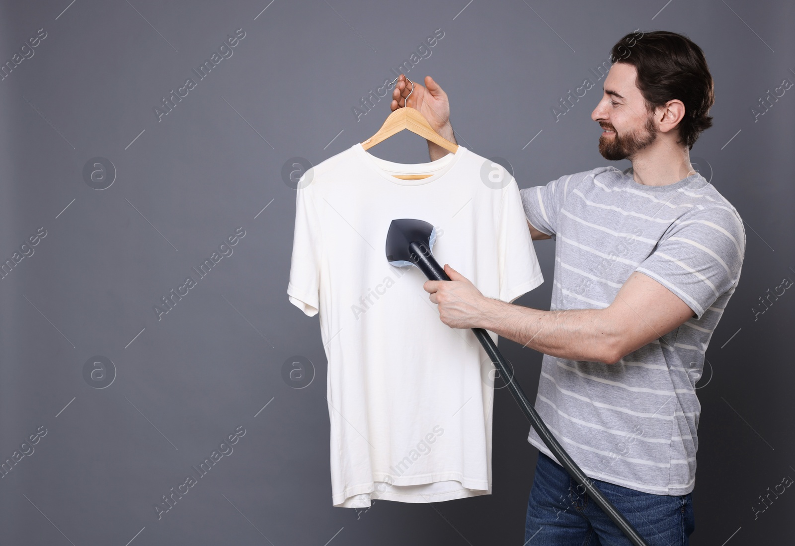 Man steaming t-shirt with stand steamer on grey background, space for text Photo of Man steaming t-shirt with stand steamer on grey background, space for text