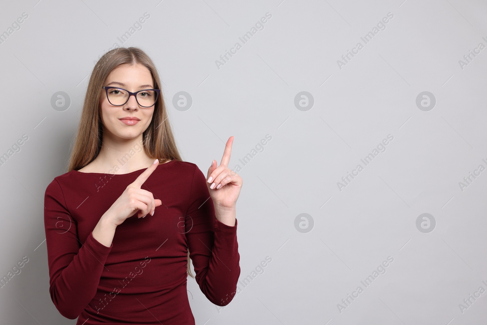 Teenage girl pointing at something on light grey background. Space for text Photo of Teenage girl pointing at something on light grey background. Space for text