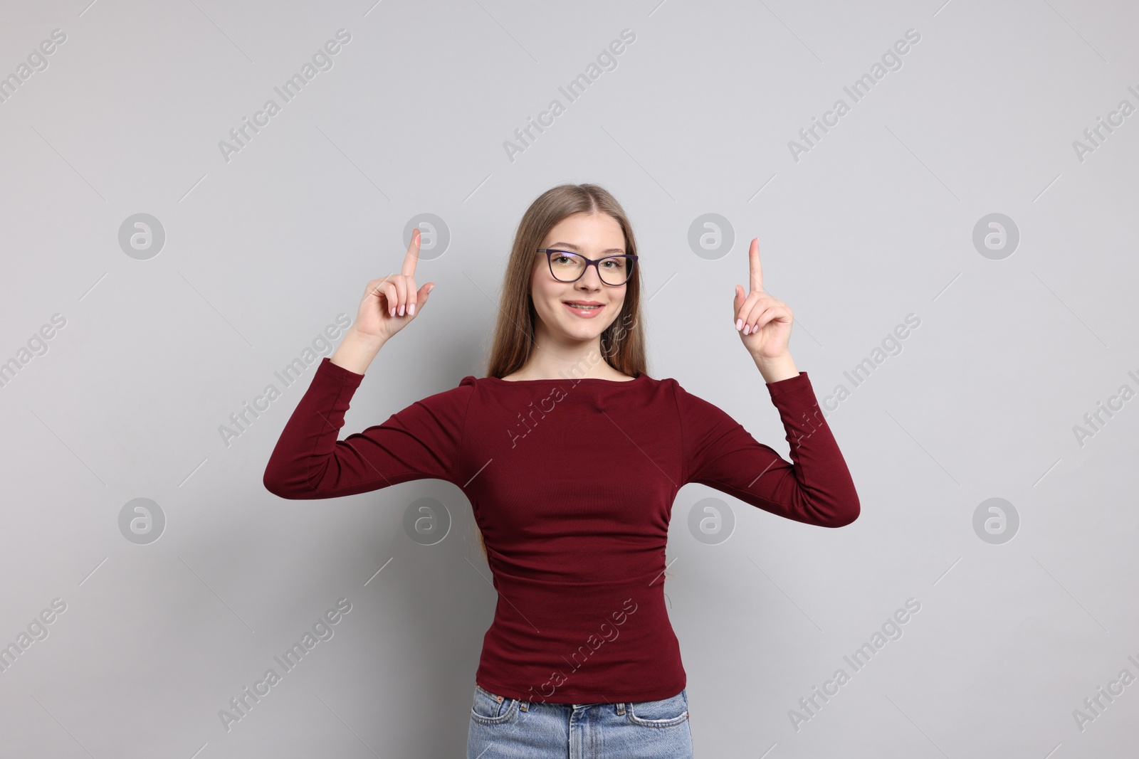 Teenage girl pointing at something on light grey background Photo of Teenage girl pointing at something on light grey background