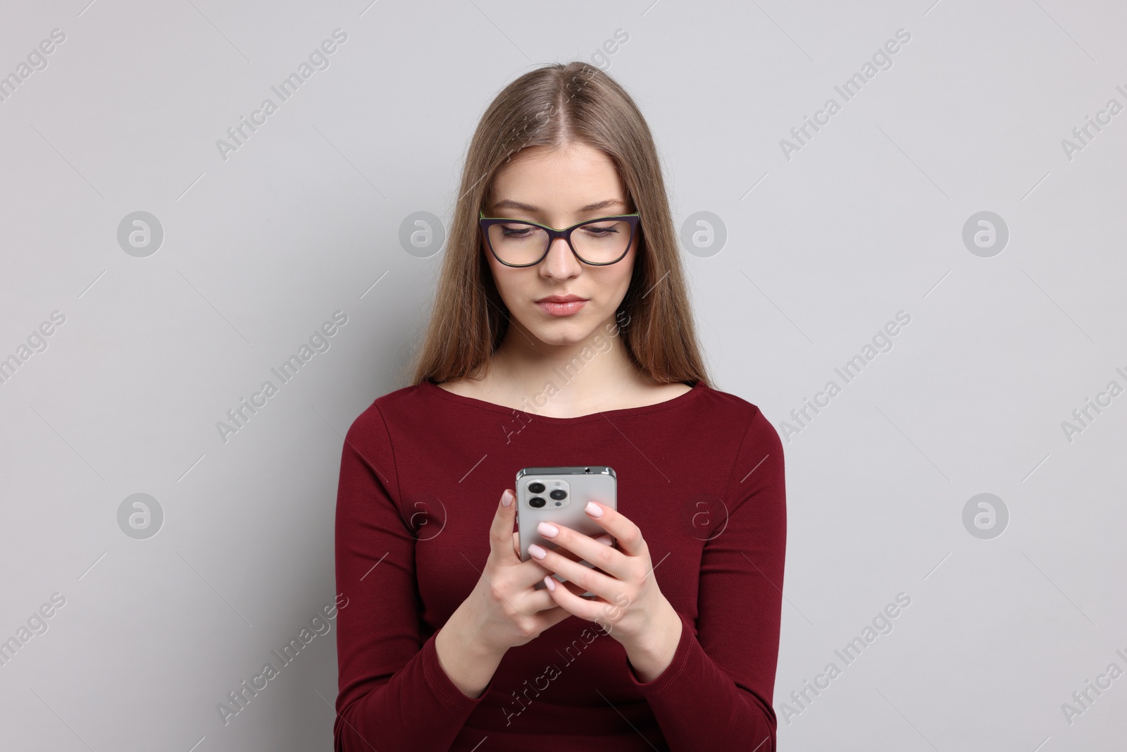 Teenage girl with smartphone on light grey background Photo of Teenage girl with smartphone on light grey background