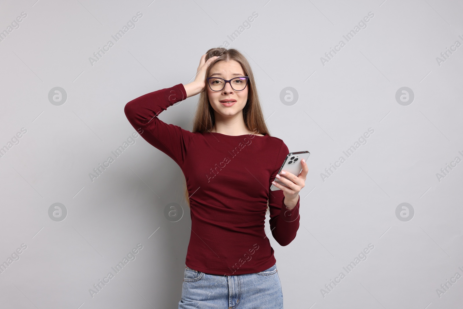 Teenage girl with smartphone on light grey background Photo of Teenage girl with smartphone on light grey background