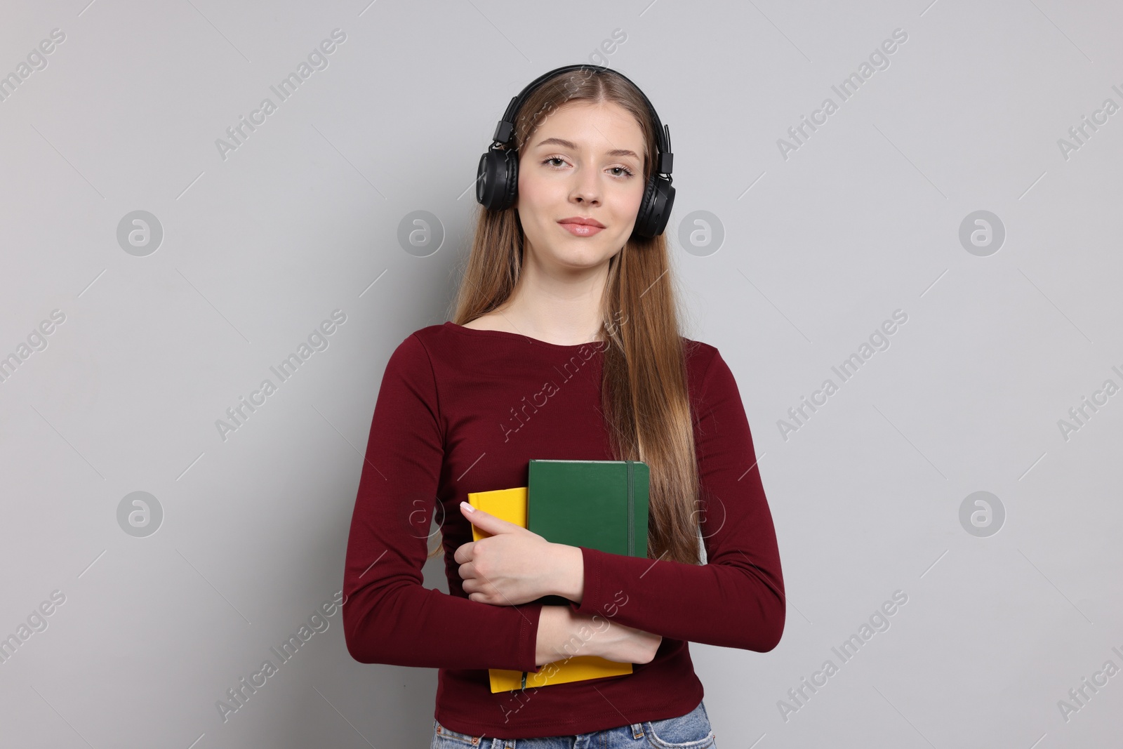 Teenage girl with headphones and notebooks on light grey background Photo of Teenage girl with headphones and notebooks on light grey background