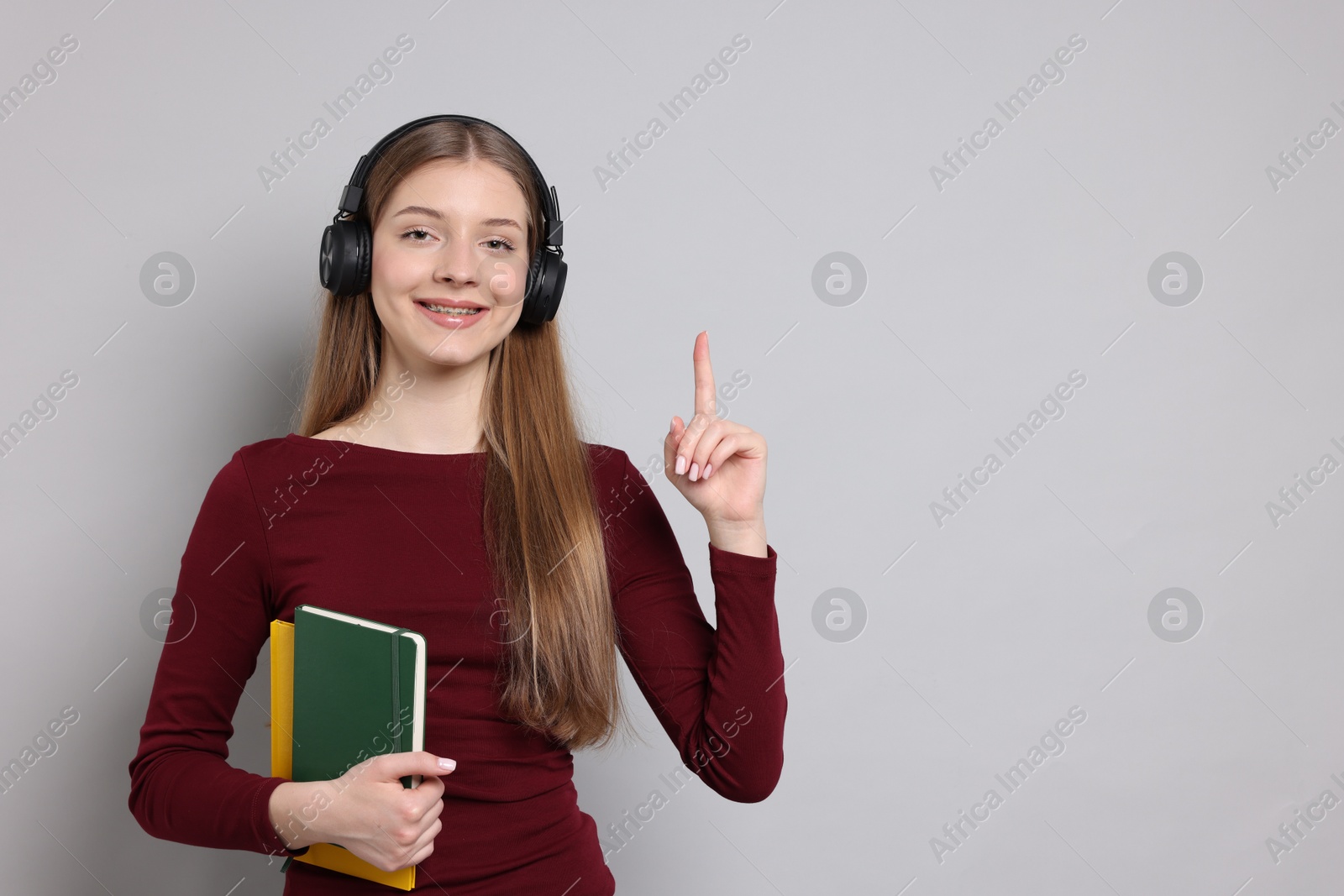 Teenage girl with headphones and notebooks on light grey background. Space for text Photo of Teenage girl with headphones and notebooks on light grey background. Space for text