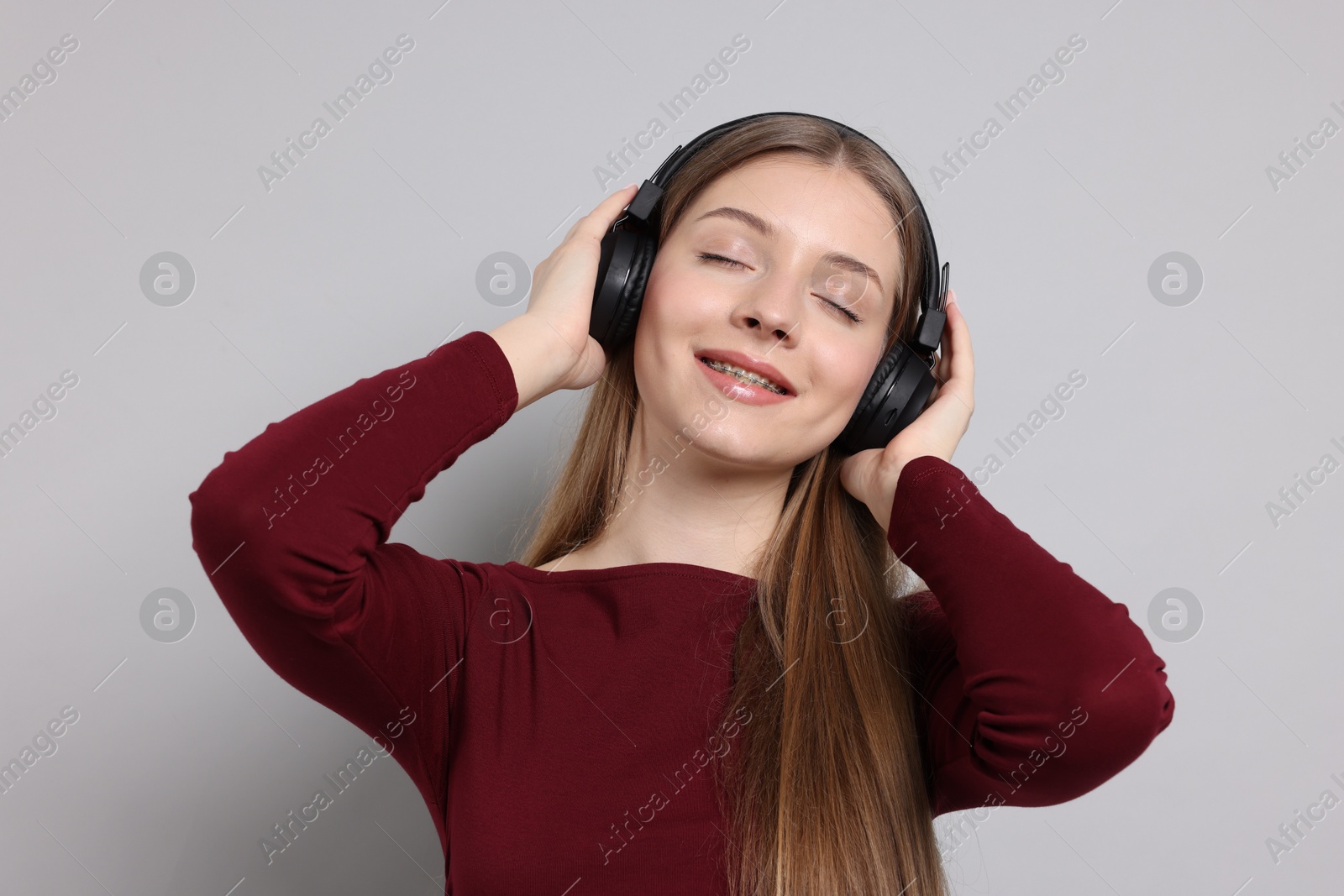 Teenage girl listening to music on light grey background Photo of Teenage girl listening to music on light grey background