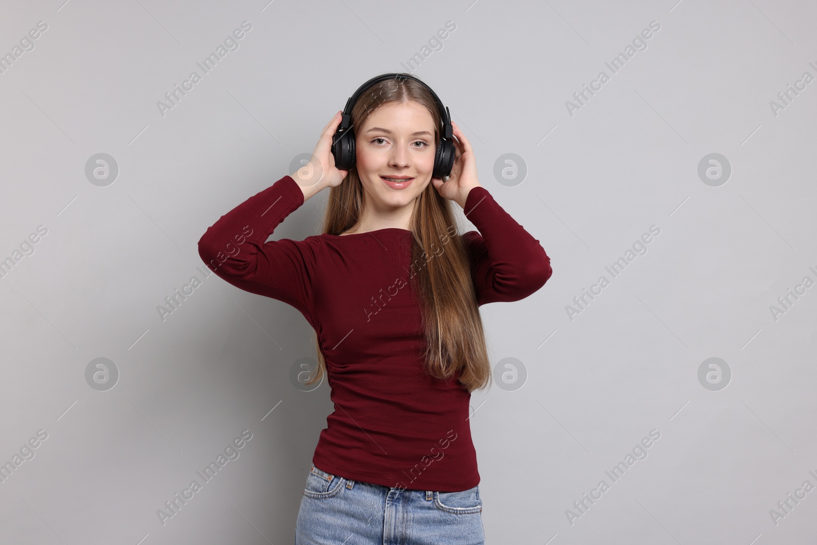 Teenage girl listening to music on light grey background Photo of Teenage girl listening to music on light grey background