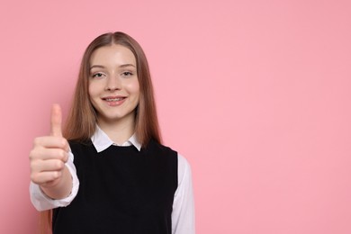 Photo of Teenage girl showing thumbs up on light pink background. Space for text