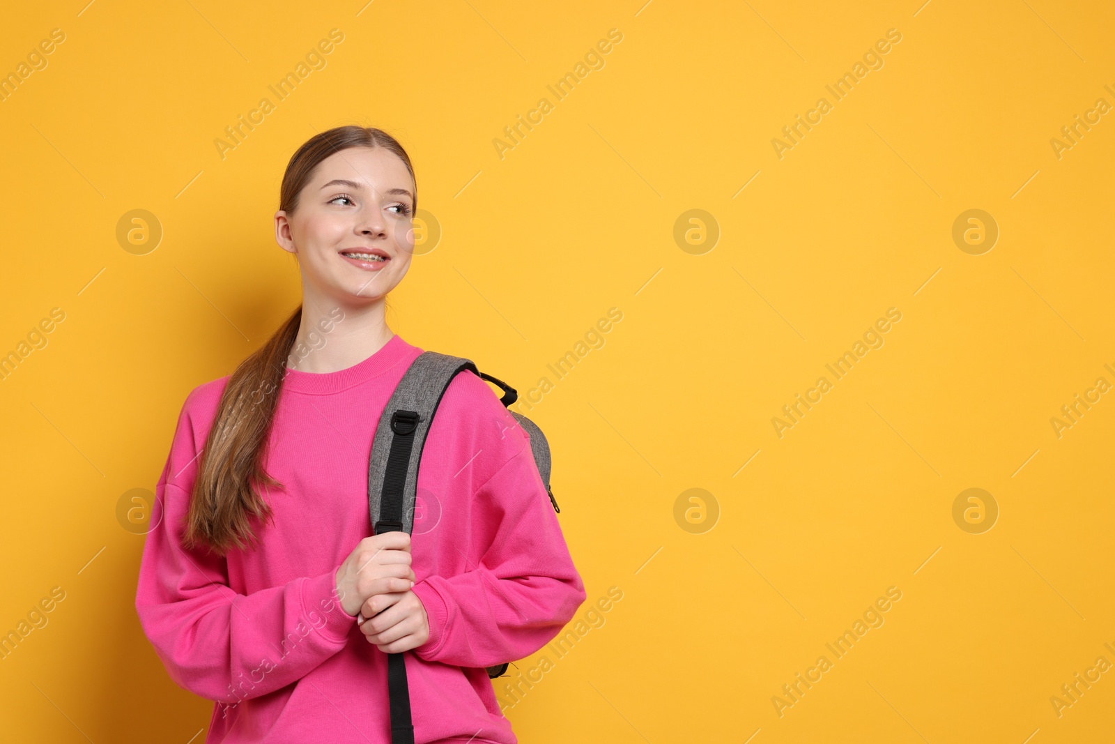 Photo of Teenage girl with backpack on yellow background. Space for text