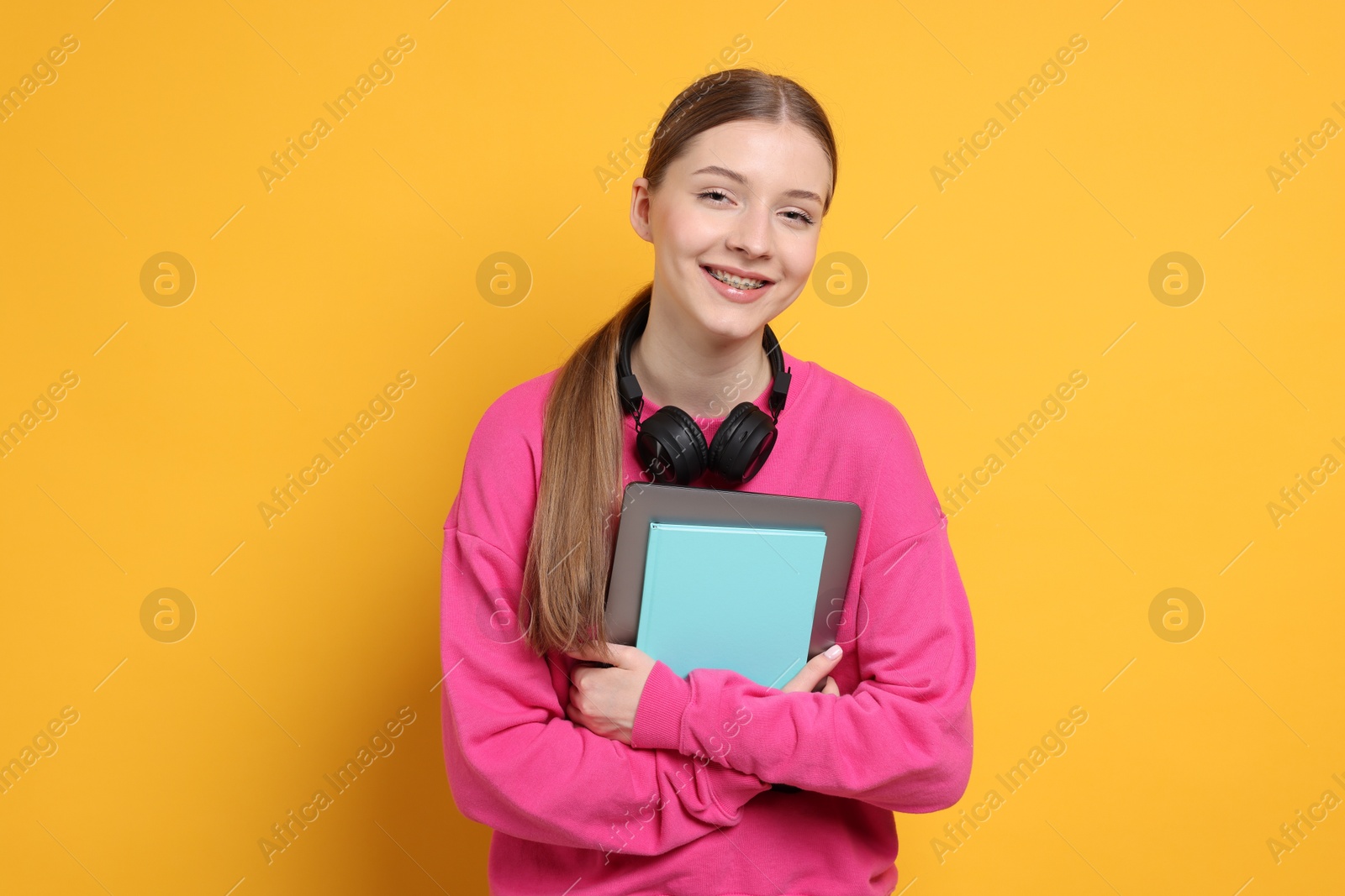 Photo of Teenage girl with laptop, notebook and headphones on yellow background