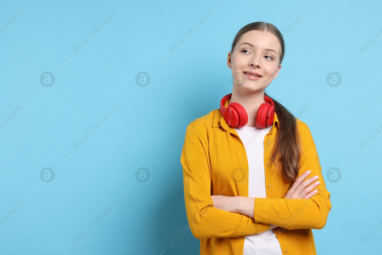 Photo of Teenage girl with headphones on light blue background. Space for text