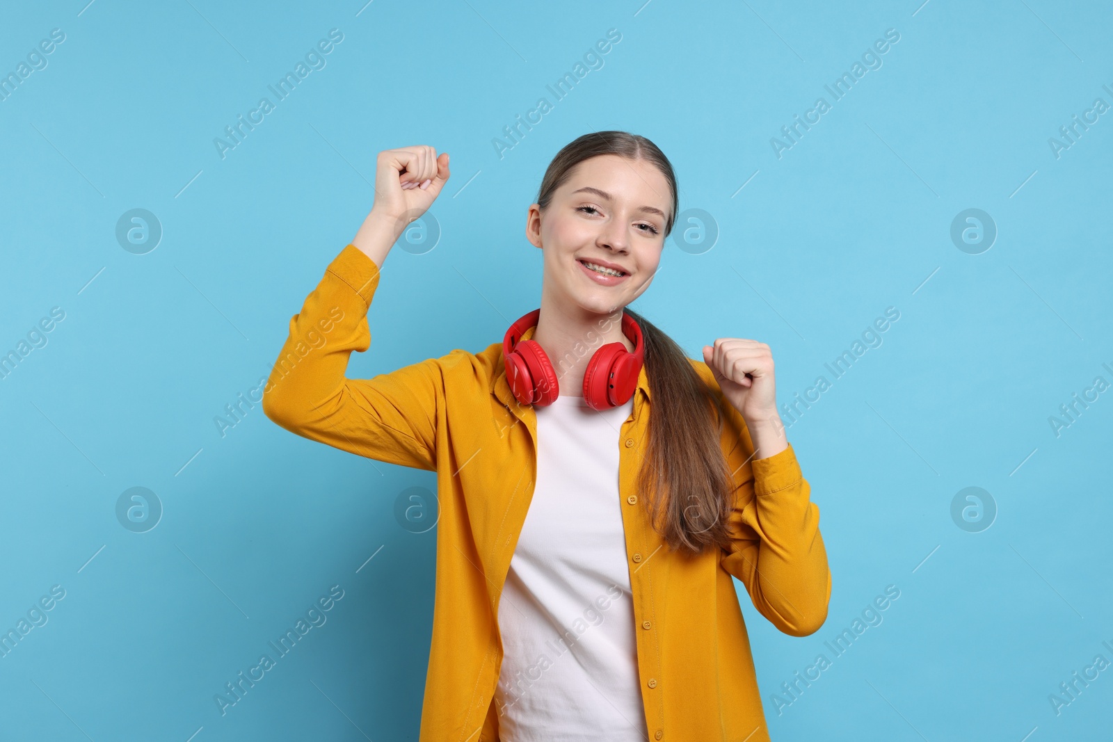 Photo of Excited teenage girl with headphones on light blue background