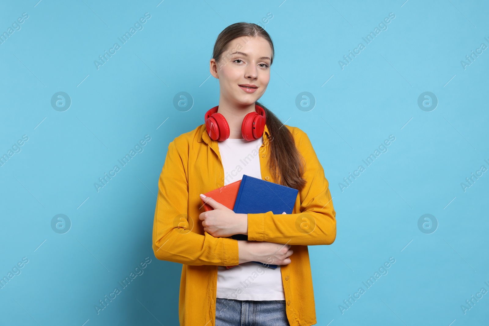 Photo of Teenage girl with headphones and notebooks on light blue background