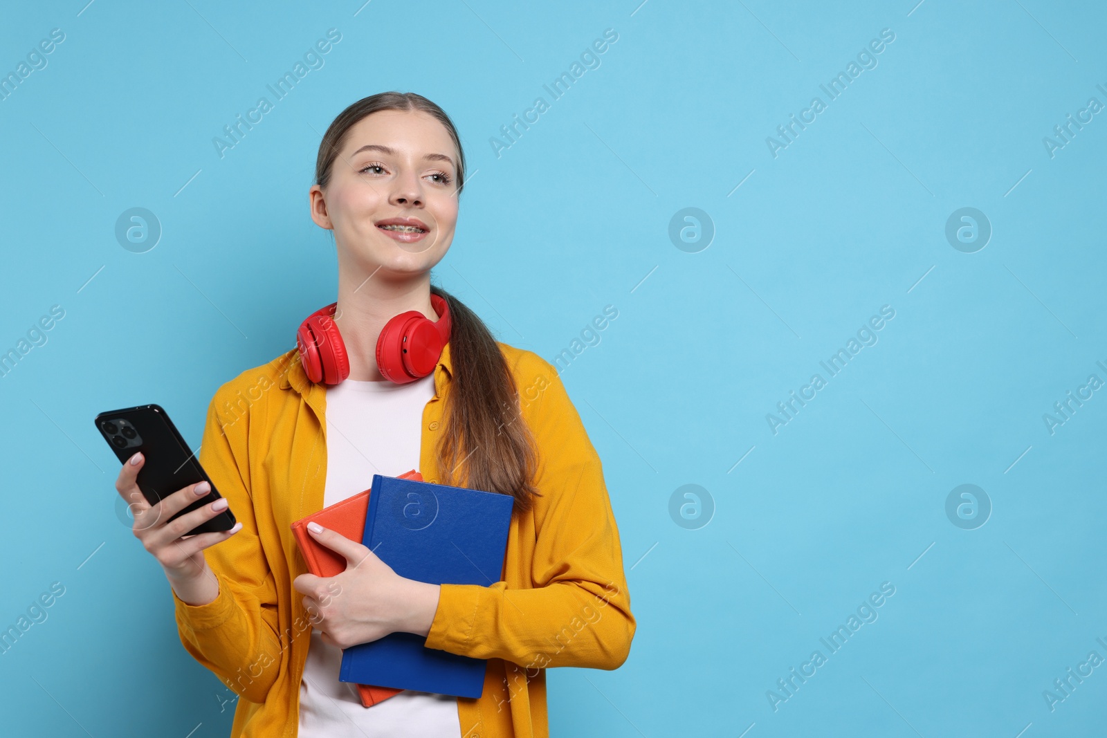 Photo of Teenage girl with headphones, smartphone and notebooks on light blue background. Space for text