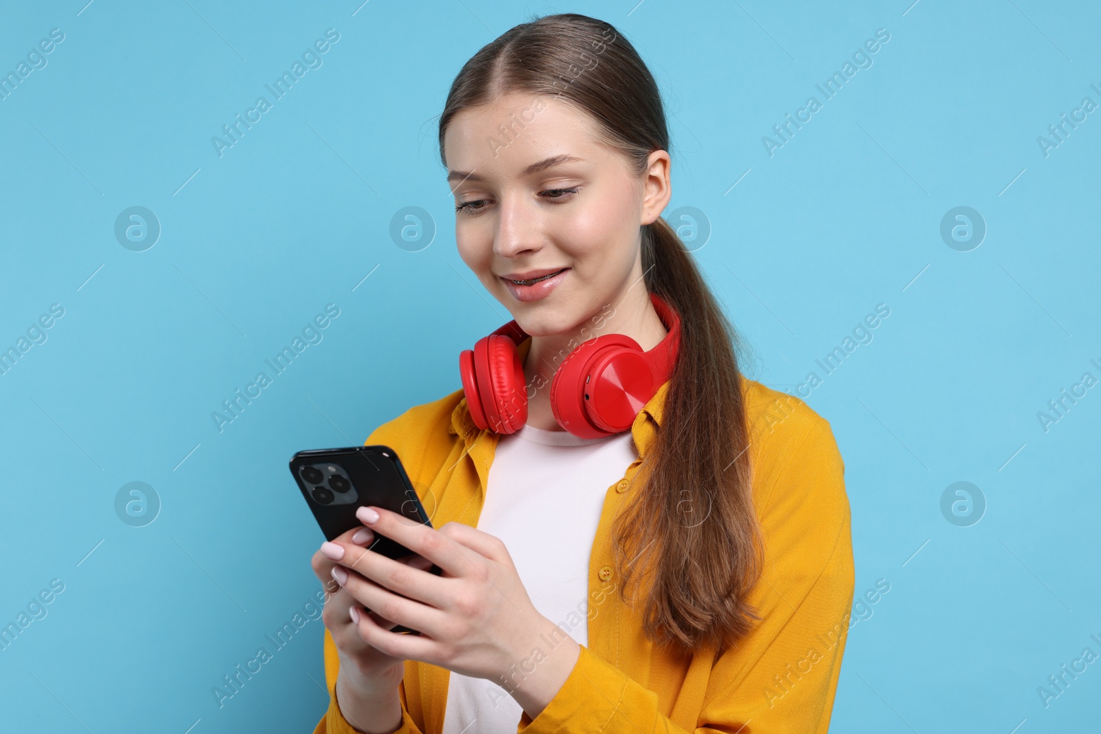 Photo of Teenage girl with headphones and smartphone on light blue background