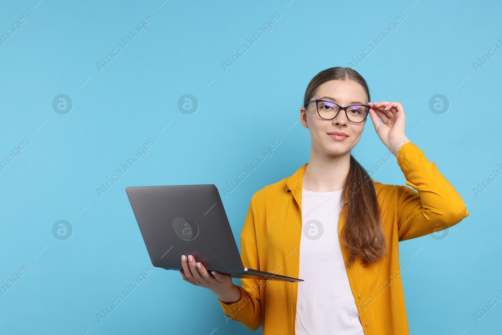 Photo of Teenage girl with laptop on light blue background. Space for text