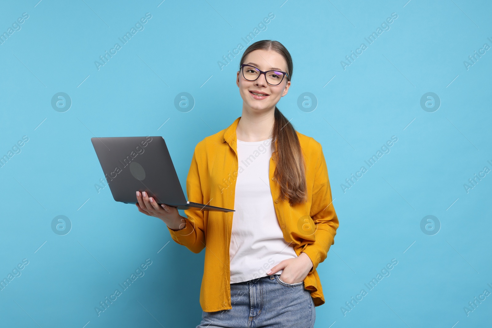 Teenage girl with laptop on light blue background Photo of Teenage girl with laptop on light blue background