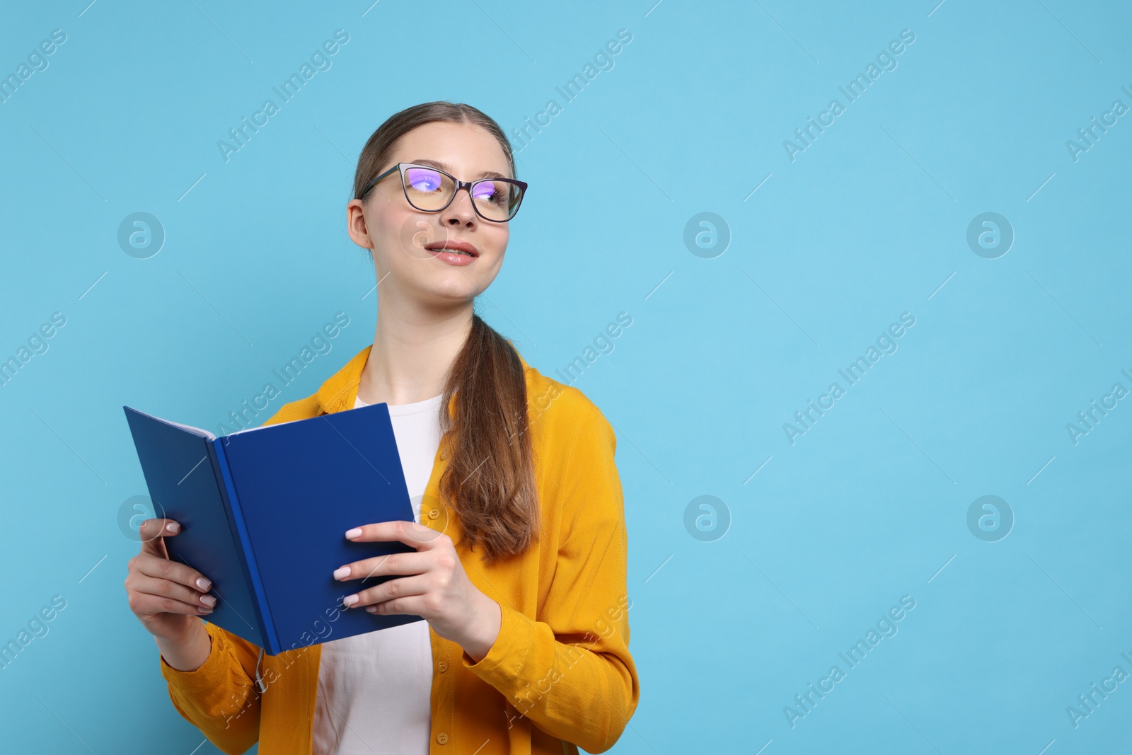 Photo of Teenage girl with book on light blue background. Space for text